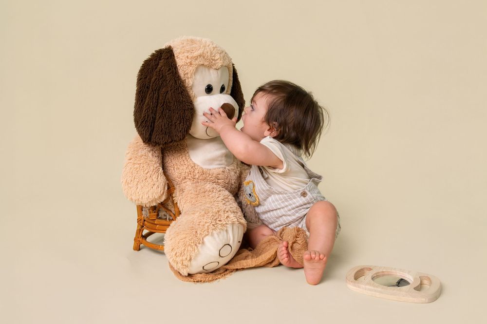 A small child interacts with a large plush puppy toy on a neutral background.
