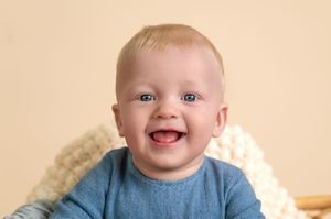 A happy baby with bright blue eyes and rosy cheeks smiles joyfully at the camera.