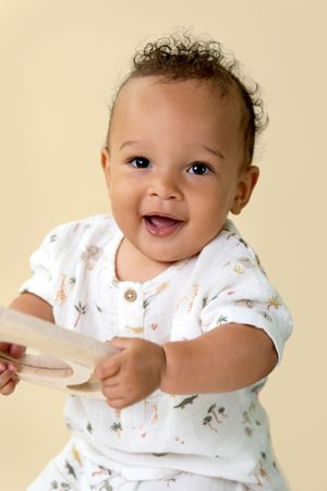 A happy baby wearing a white patterned outfit lying on a cream colored background.