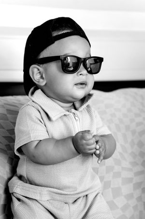 A baby wearing sunglasses and a light-colored outfit poses in a series of black and white photos.