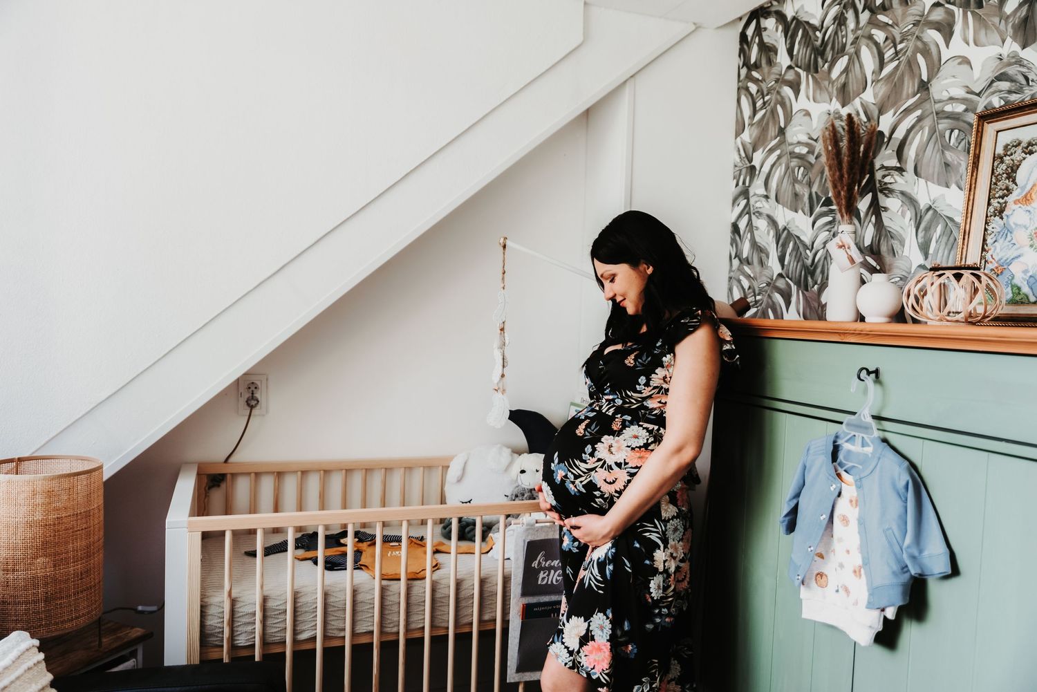 An expectant mother looks at nursery items next to a wooden crib.