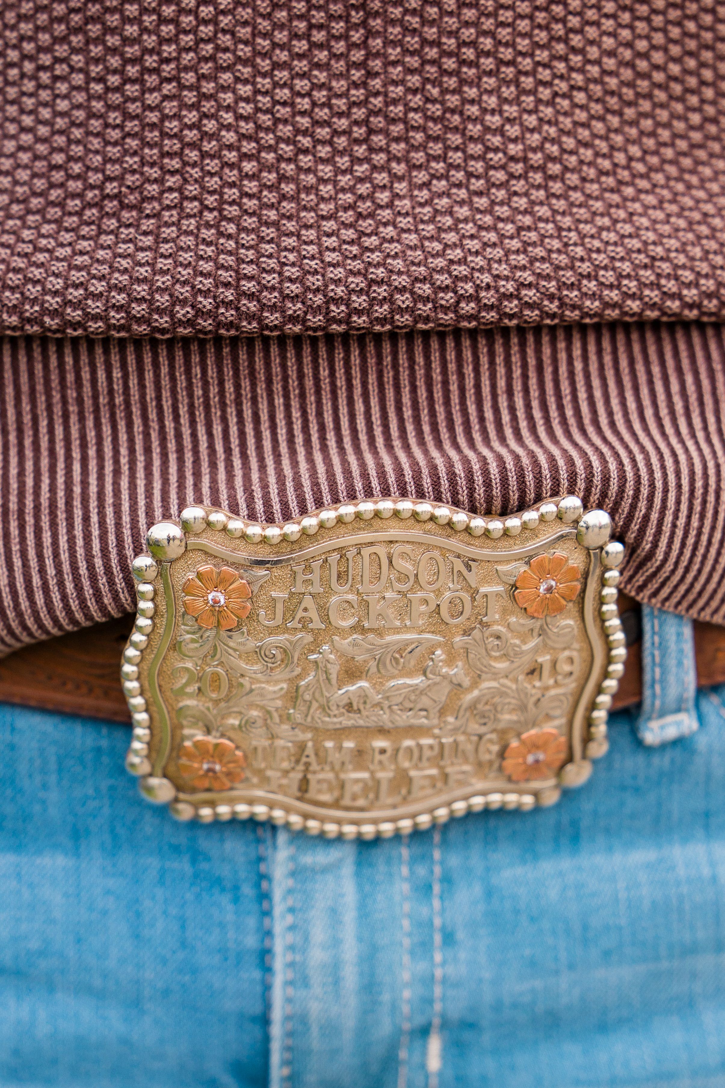 Close-up of ornate gold Hudson Jackpot 2019 Calf Roping belt buckle on denim jeans.
