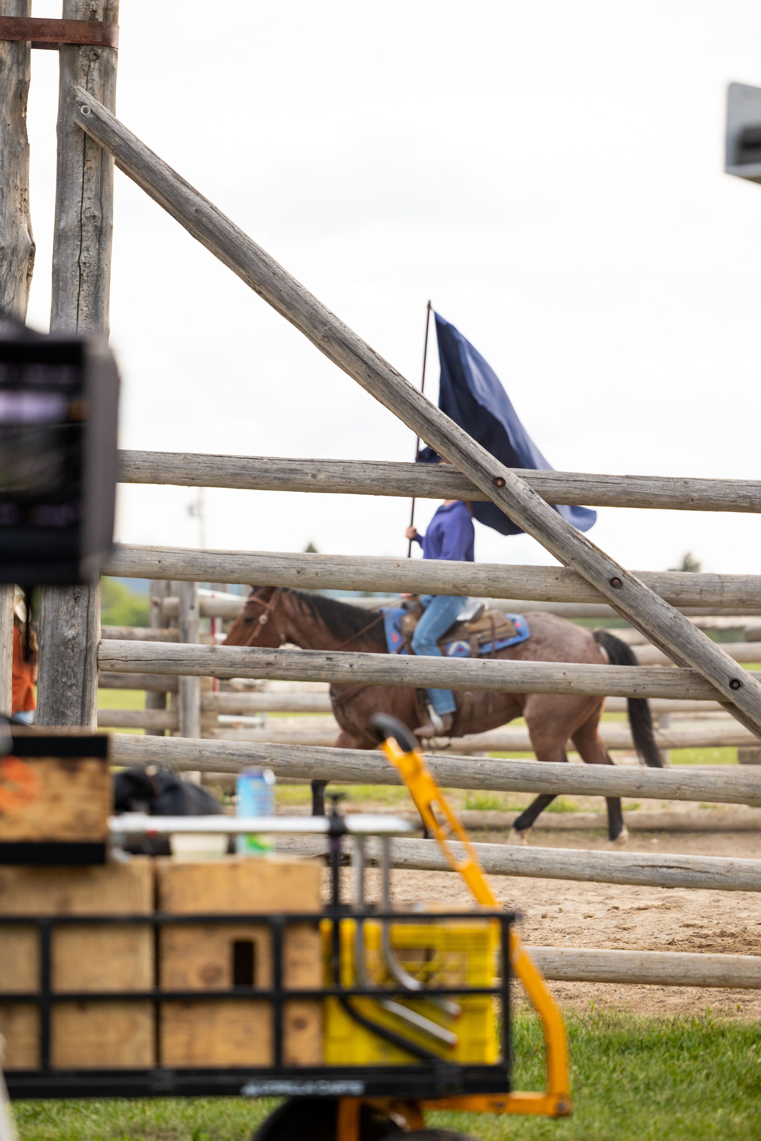Horse and rider visible through rustic wooden fence rails on film production set.