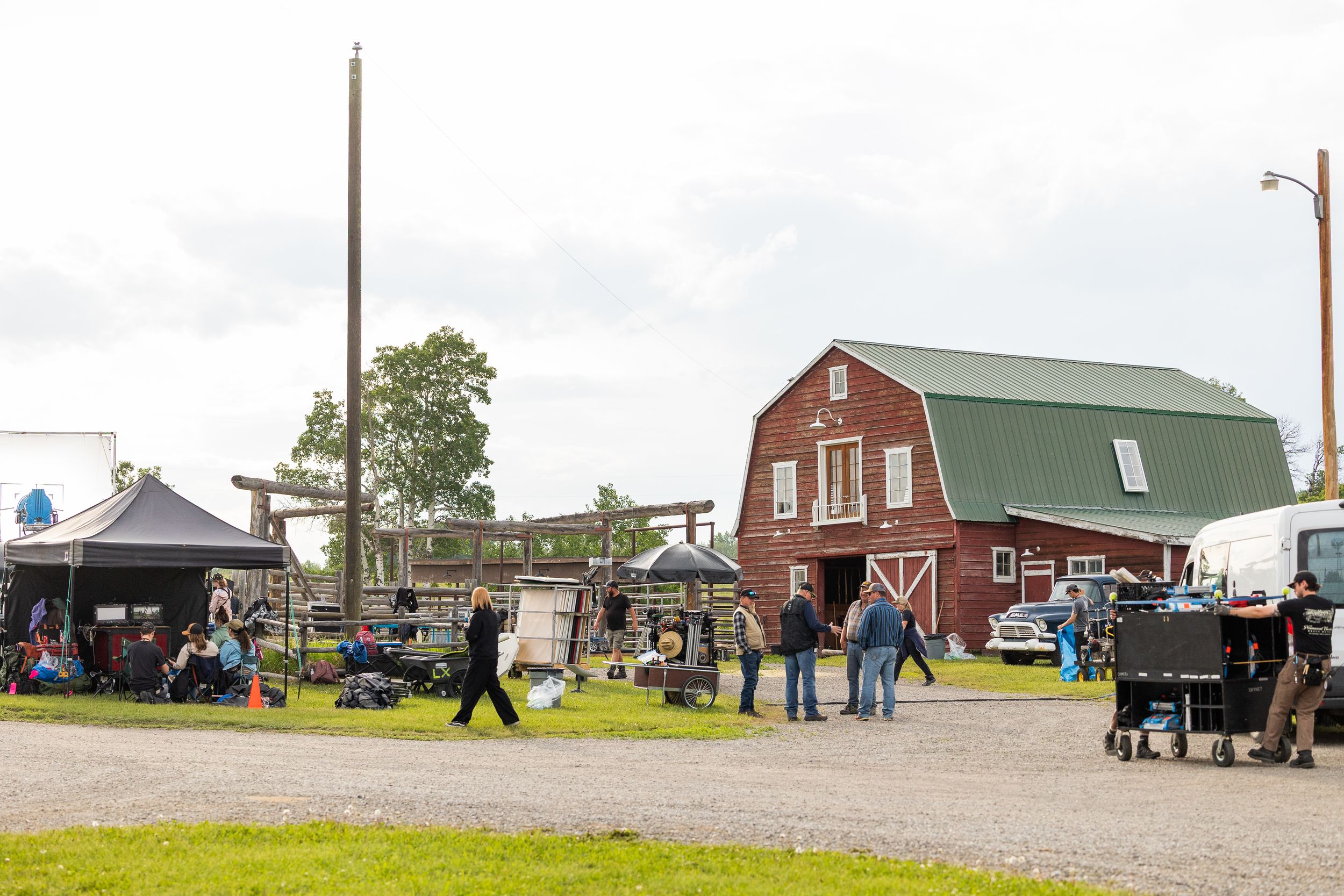 Film crew working outside red barn on rural ranch production set on overcast day.