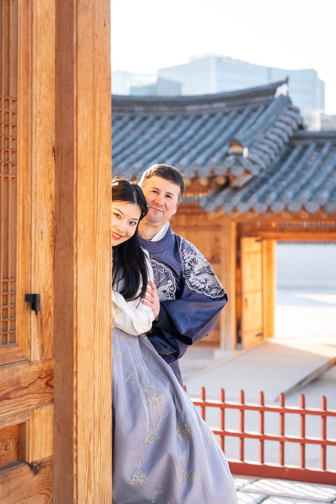 Person wearing traditional Korean hanbok poses playfully at a traditional wooden hanok building in Korea.
