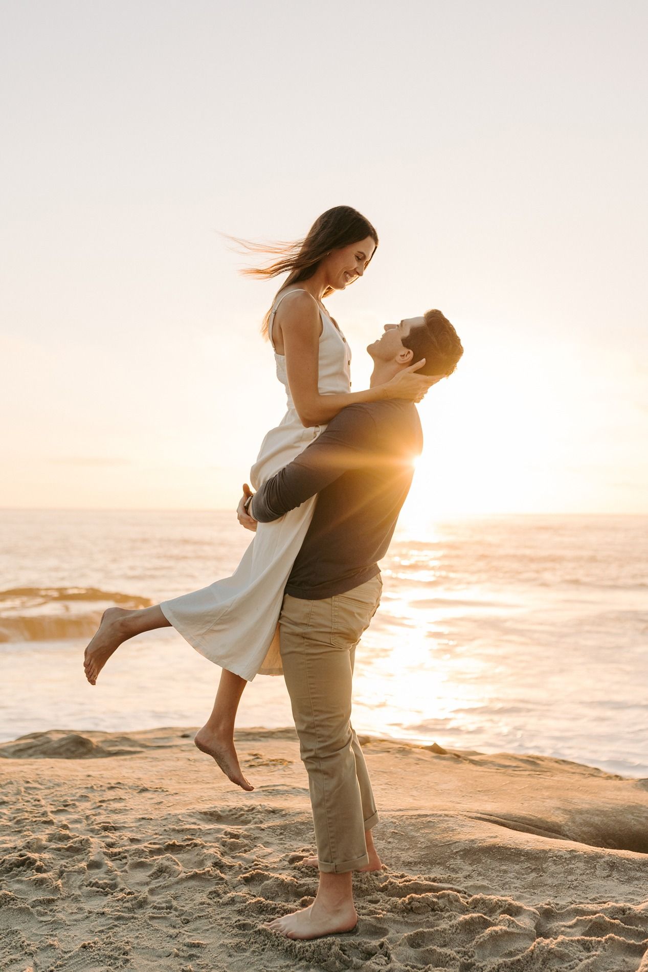A romantic couple twirls on a sandy beach at sunset, creating silhouettes against the golden ocean backdrop at Windansea Beach.