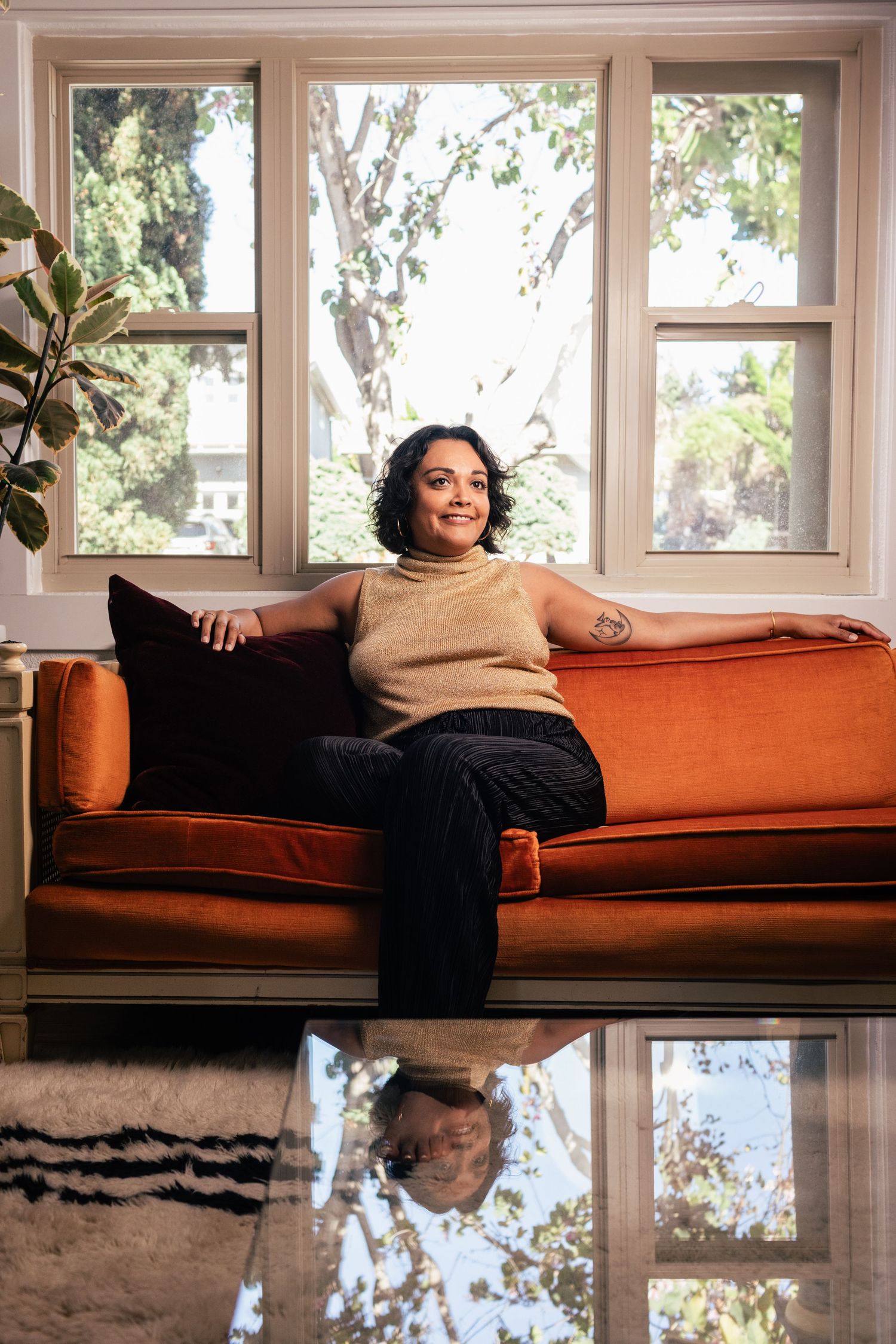 Someone relaxes on an orange couch by a bright window in a casual indoor setting.