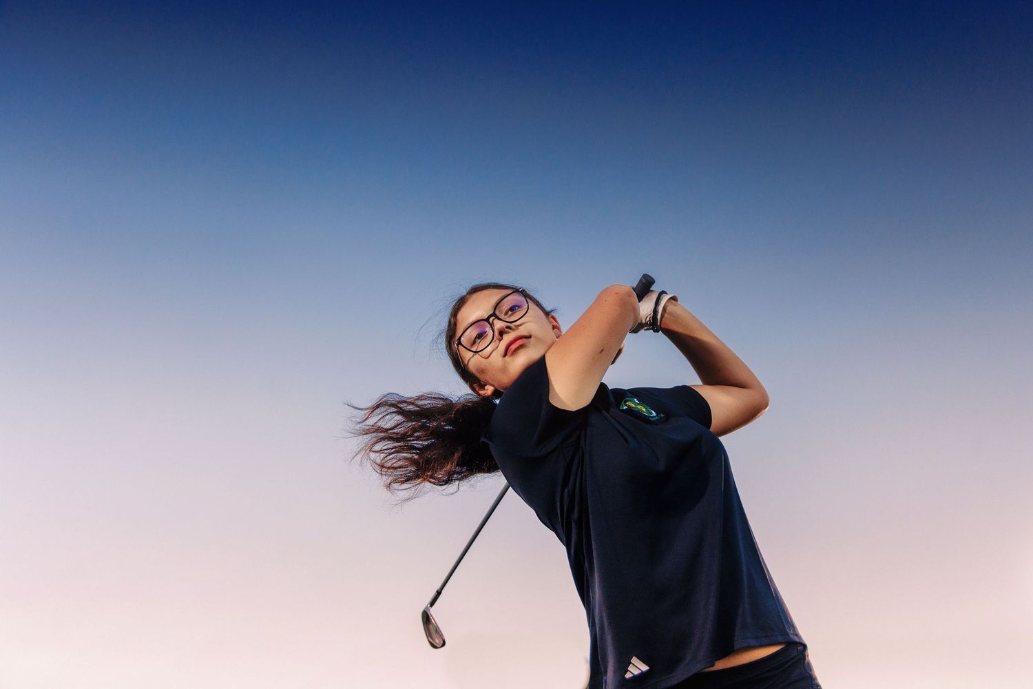 Golfer swinging club against blue sky at sunset.