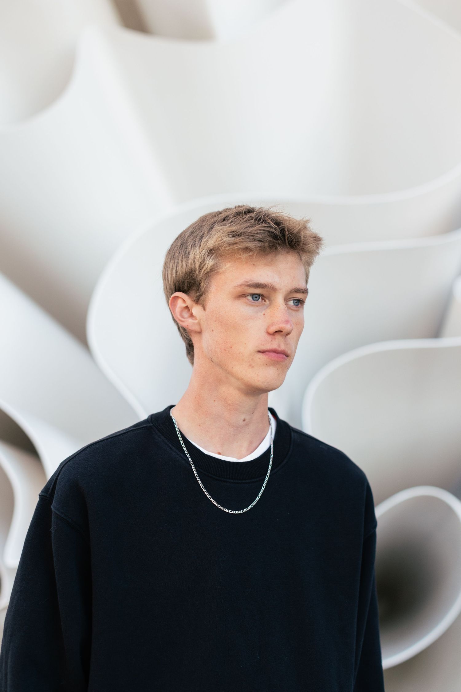 A series of four profile shots against a white background showing someone wearing a black sweater and silver necklace.