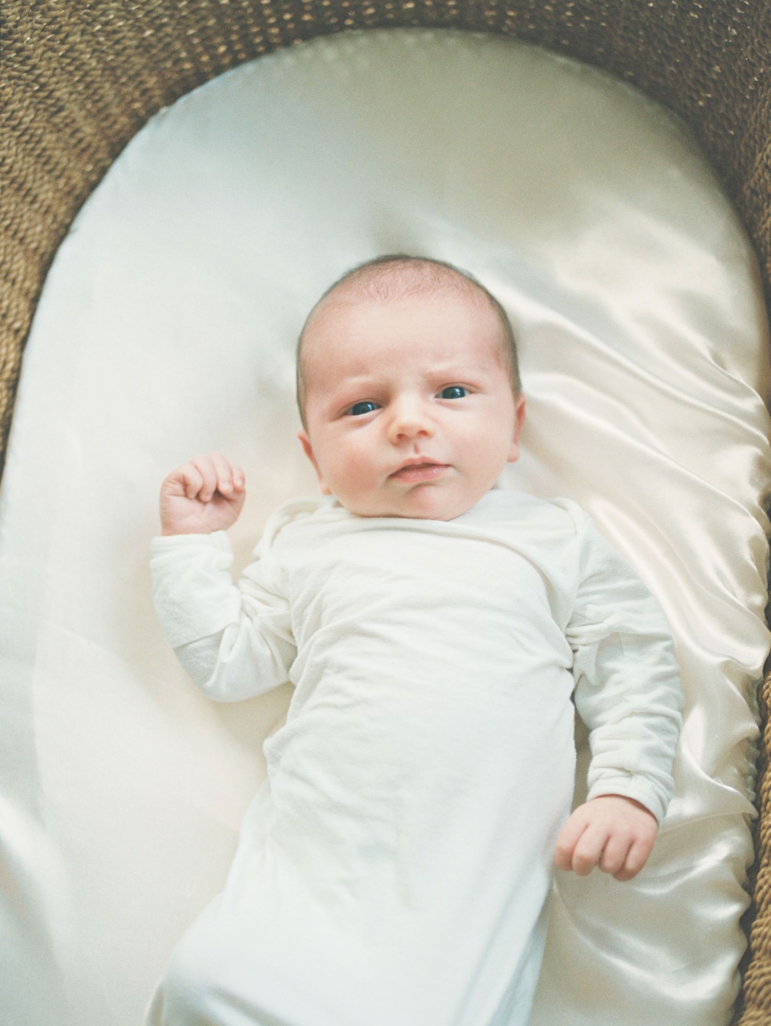 A baby wearing white clothing lies on a soft cream-colored satin blanket in a series of connected photos.