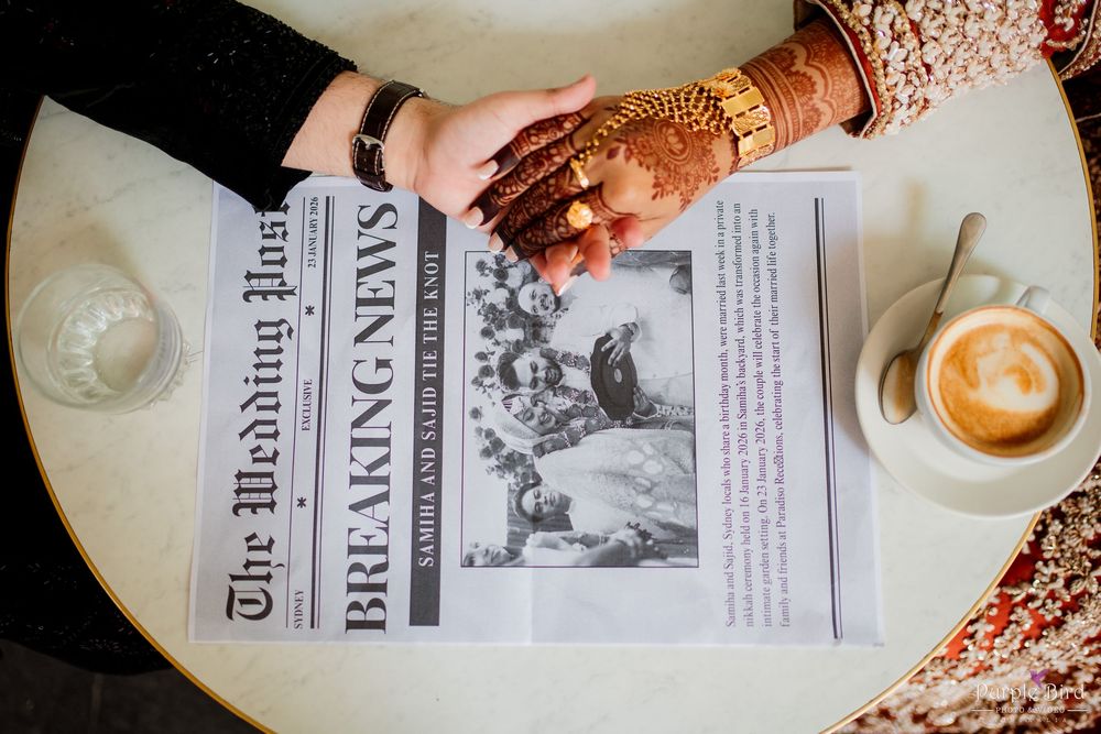 A coffee cup with latte art sits next to an open newspaper on a wooden table with scattered coffee beans.