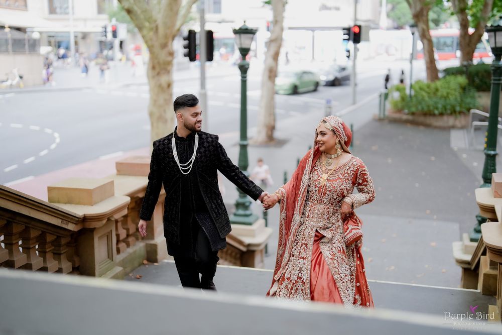 A couple walks together outdoors, with the person wearing a flowing red dress and the other in dark formal attire.