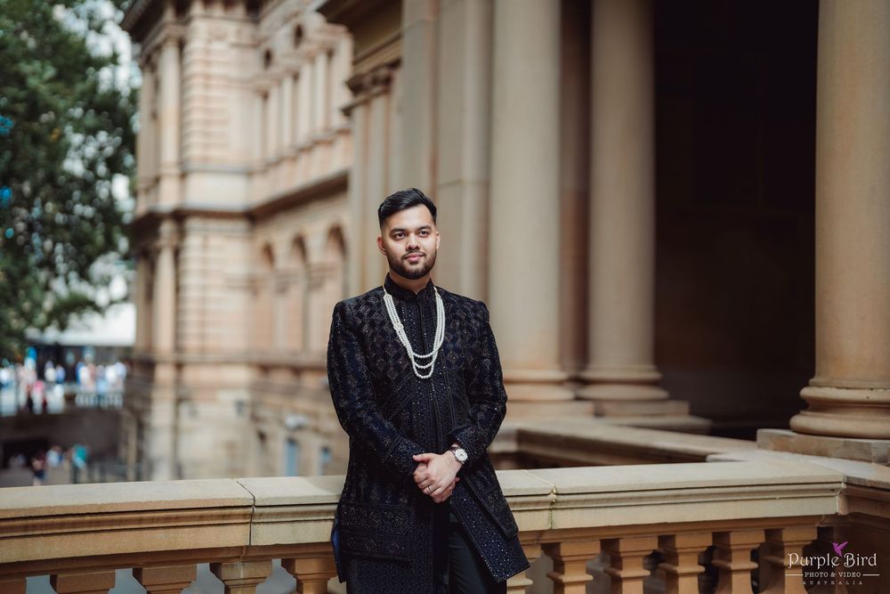 A person in a black traditional outfit stands elegantly in front of a historic stone building with classical columns.