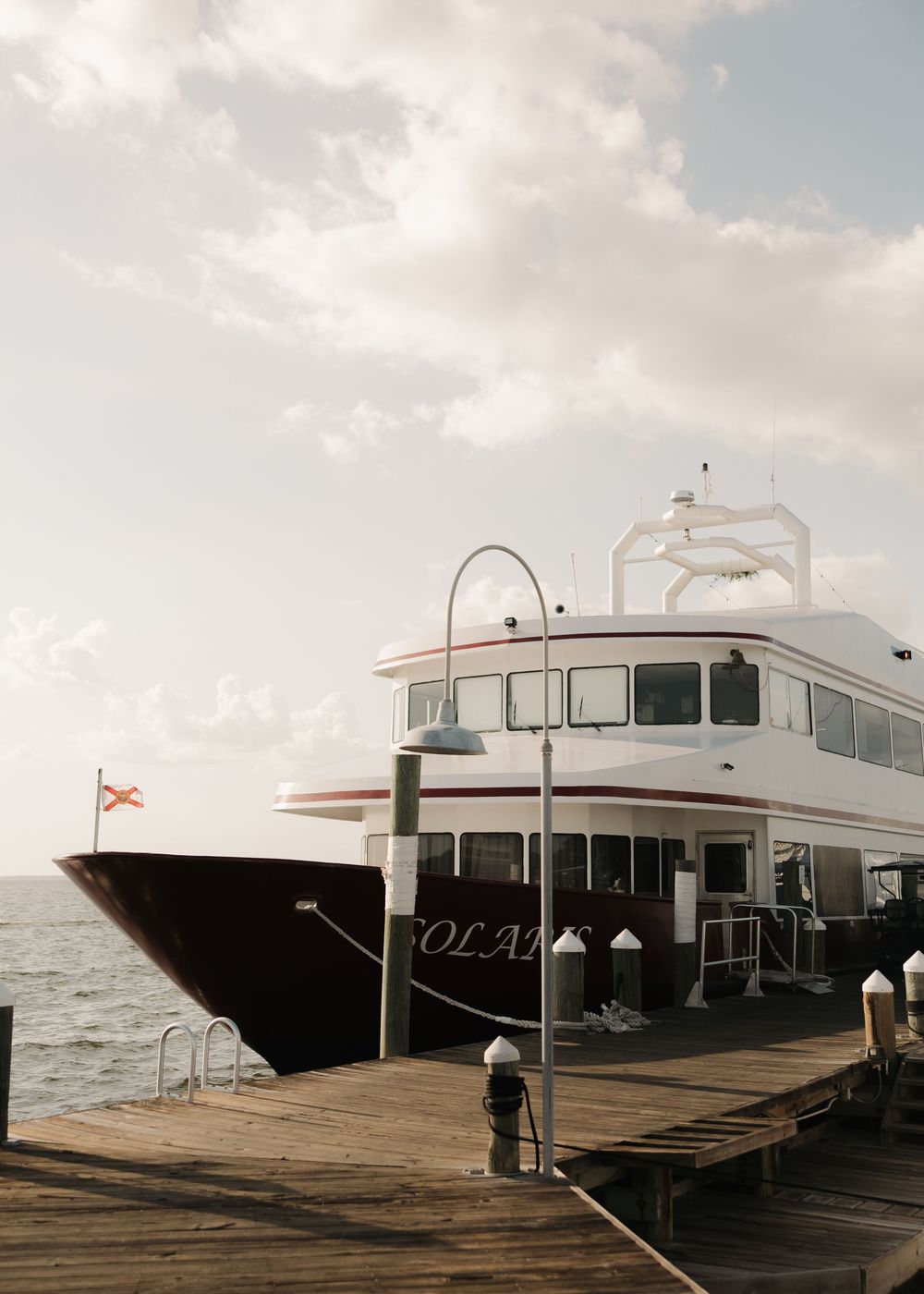 Luxury yacht docked at a wooden pier during sunset with calm waters in the background.