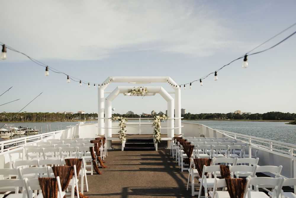 White wedding arch and chairs set up for a waterfront ceremony on a wooden dock overlooking a scenic lake.
