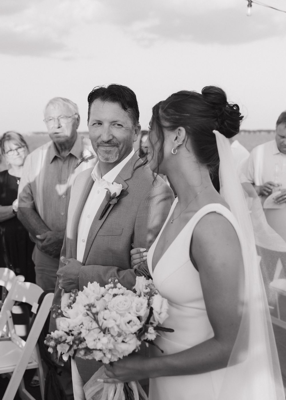 Wedding celebration on a boat deck with guests in formal attire and floral bouquets.