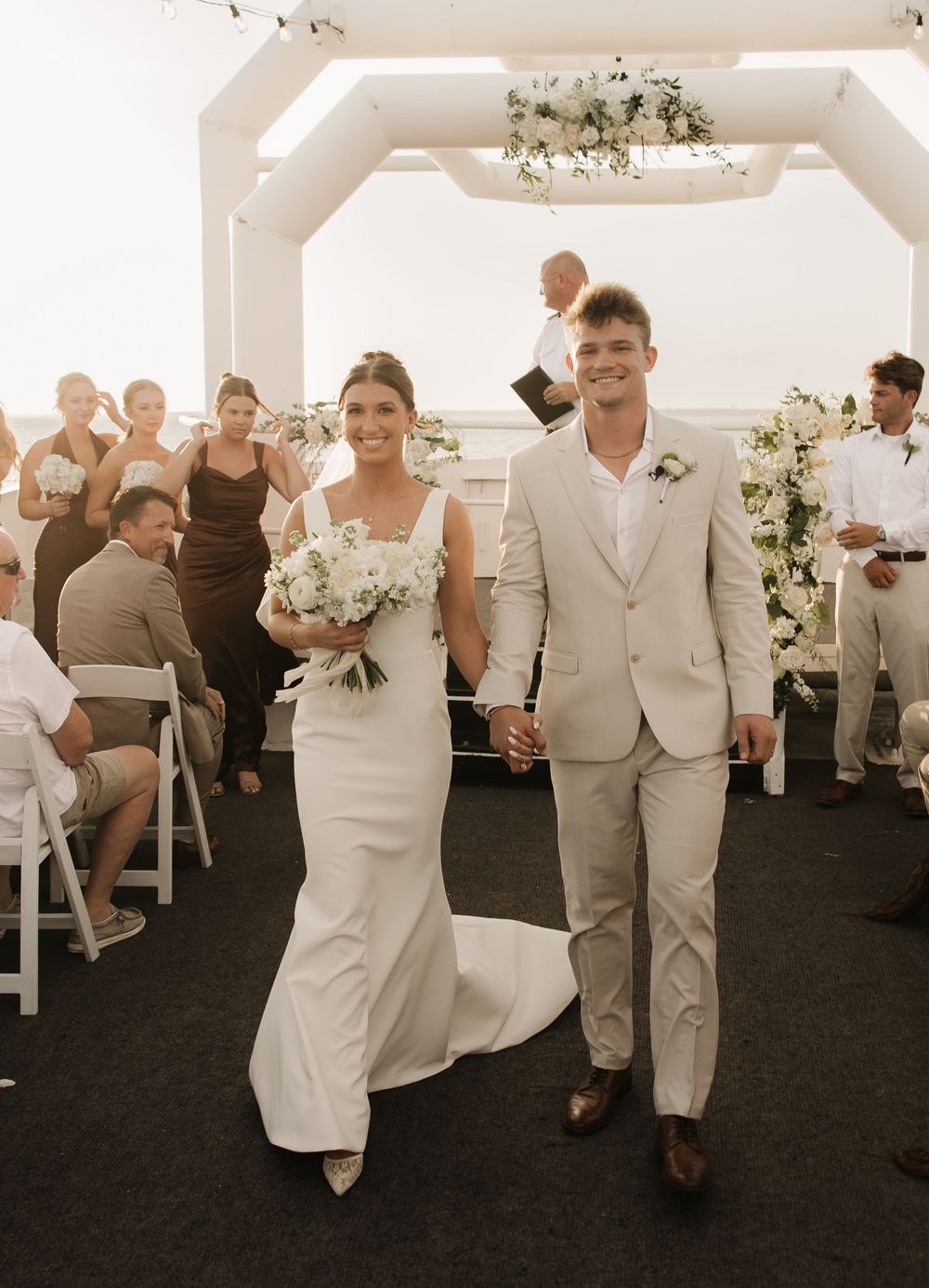 Wedding party in white and beige attire walking and celebrating in an elegant indoor venue.