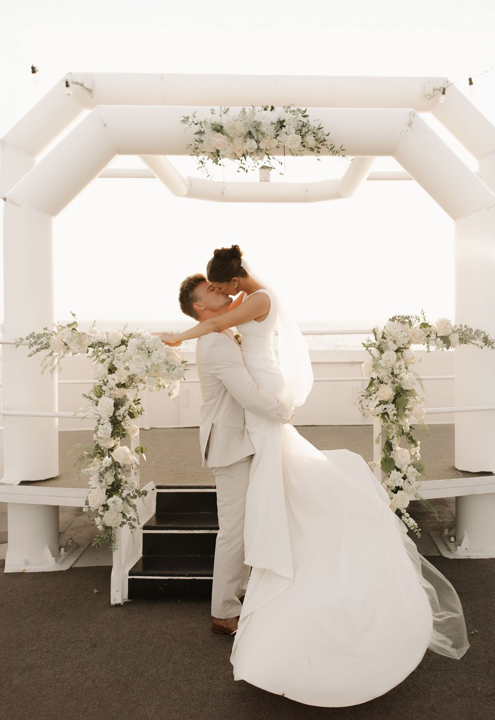 A bride in a white wedding dress twirls gracefully in a room decorated with white floral arrangements.