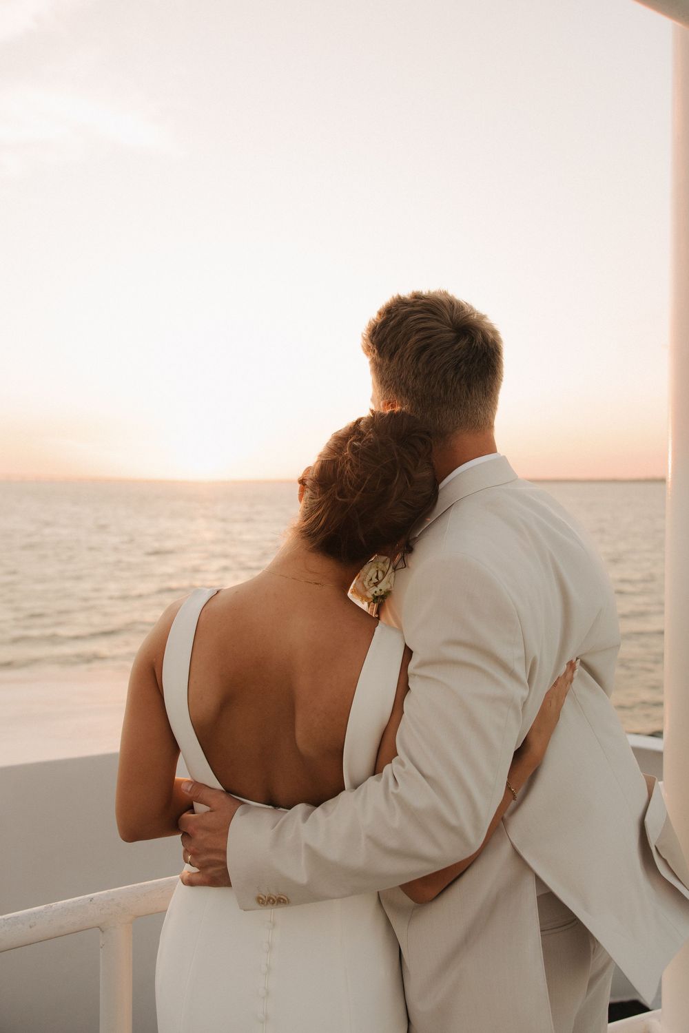 Romantic couple embraces while watching sunset over the ocean from a boat.