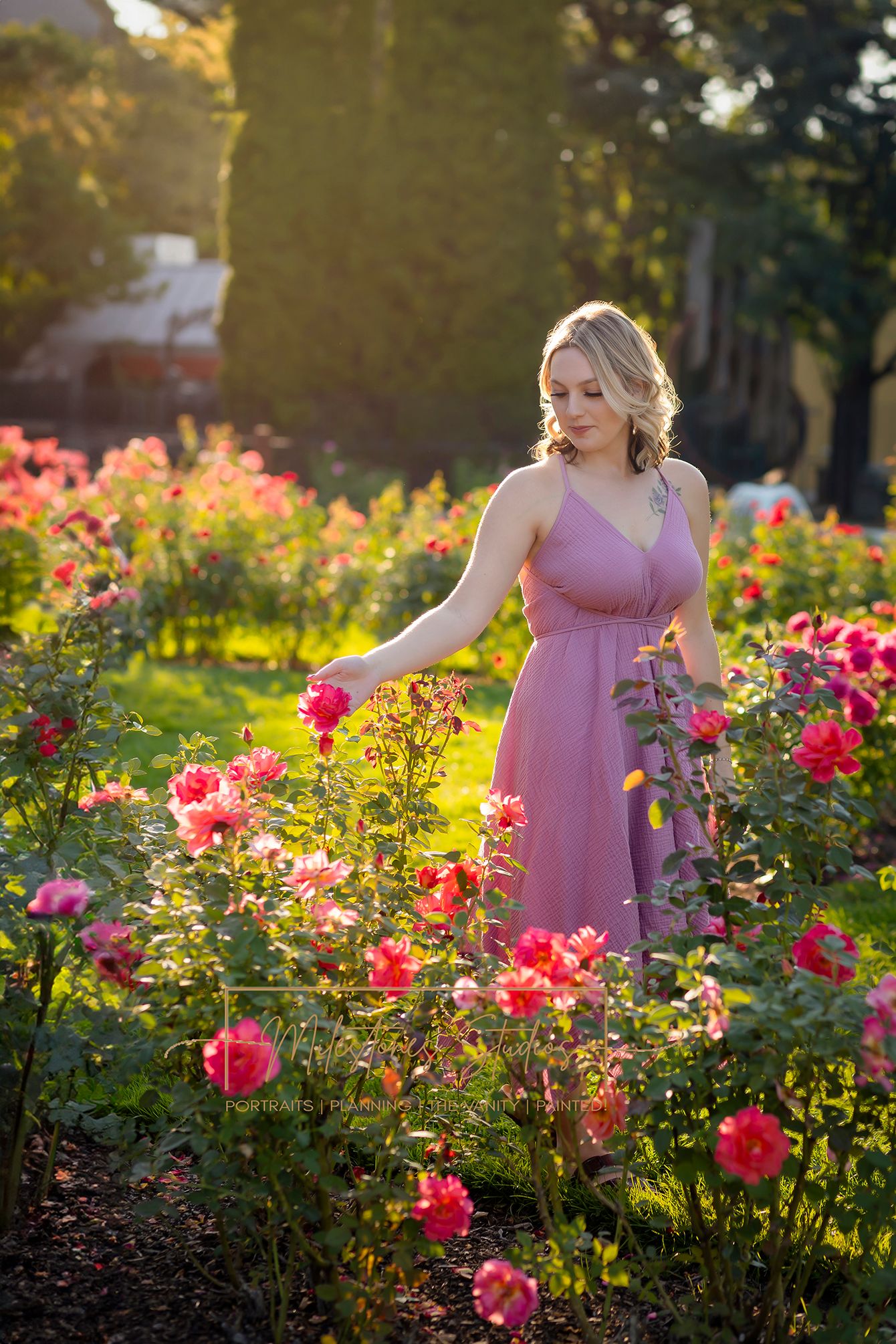 Rose Garden Julia Davis Park Boise Idaho Senior photo Girl in pink dress looking at Roses sunlight filtering through trees