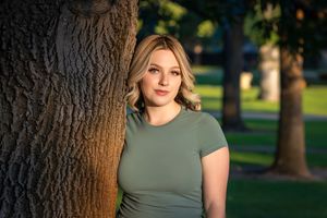 Rose Garden Julia Davis Park Boise Idaho Senior photo girl wearing green t-shirt and jeans  standing near tree with sun lighting her face