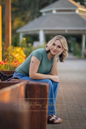 Rose Garden Julia Davis Park Boise Idaho Senior photo girl wearing green t-shirt and jeans sitting on bench leaning over with elbow on knee