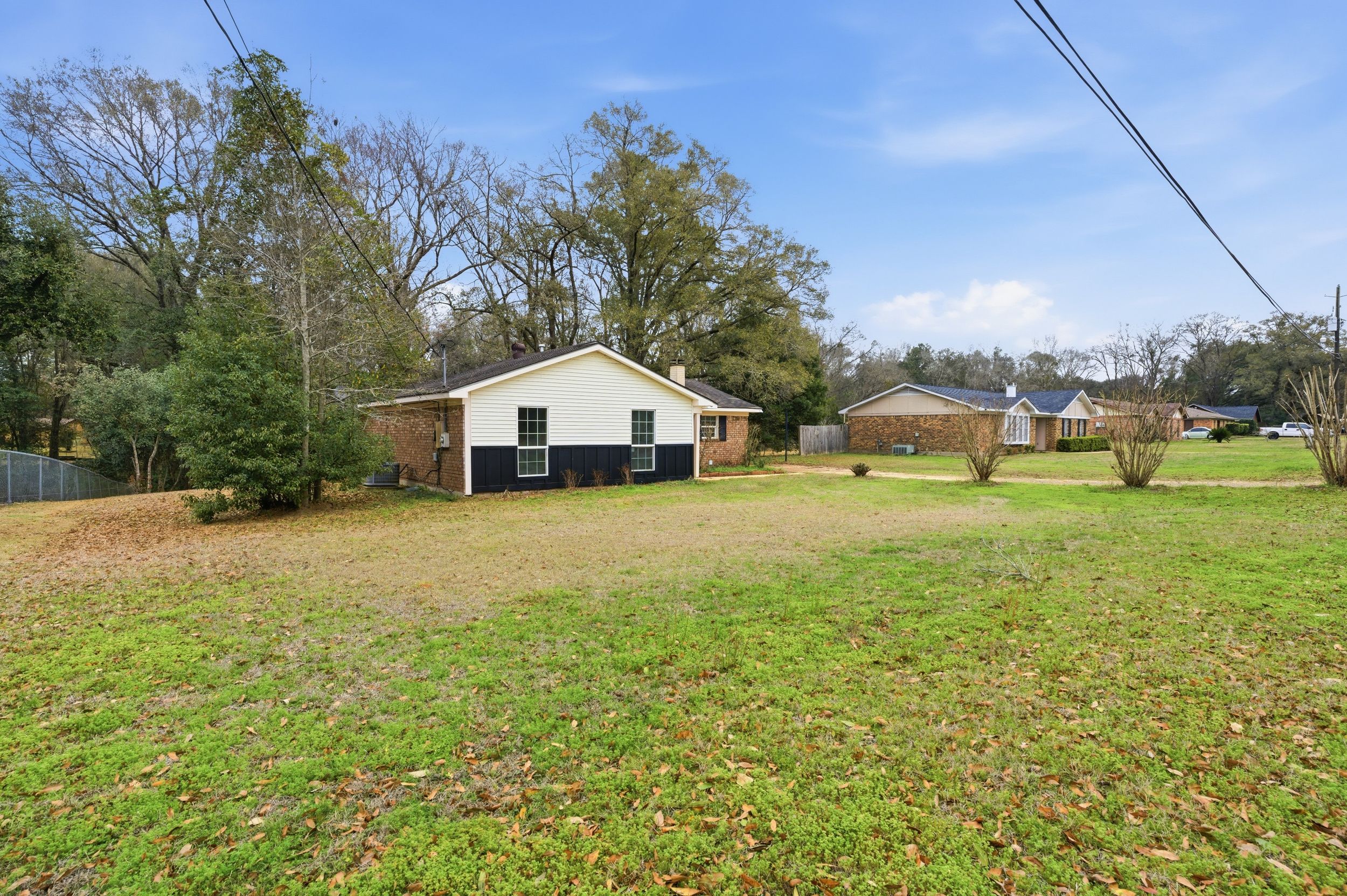 Scenic view of an undeveloped grassy lot with trees and residential homes in the background.
