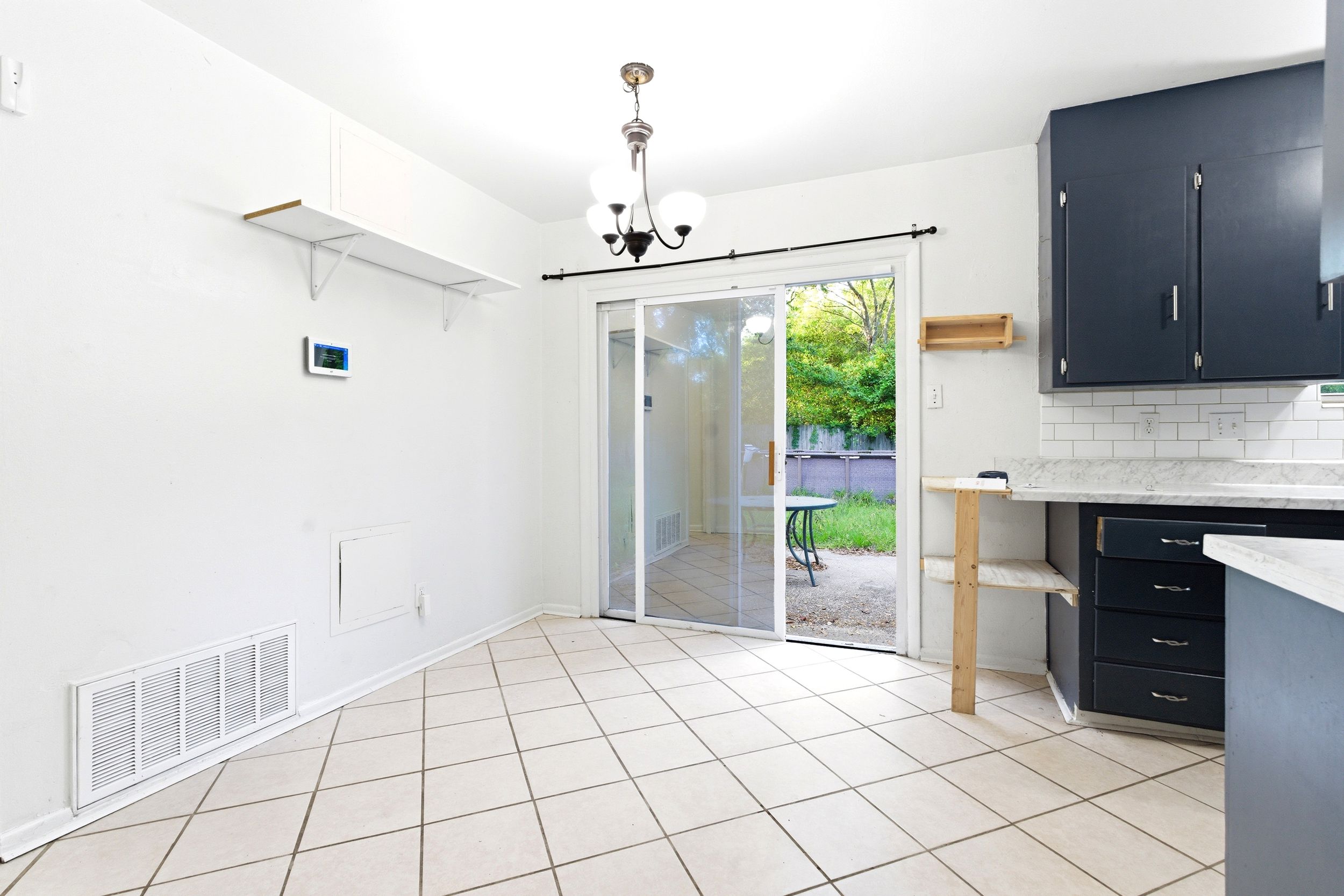 Bright kitchen dining area with tile floors, navy cabinets, subway tile backsplash, and sliding glass doors leading to a garden.