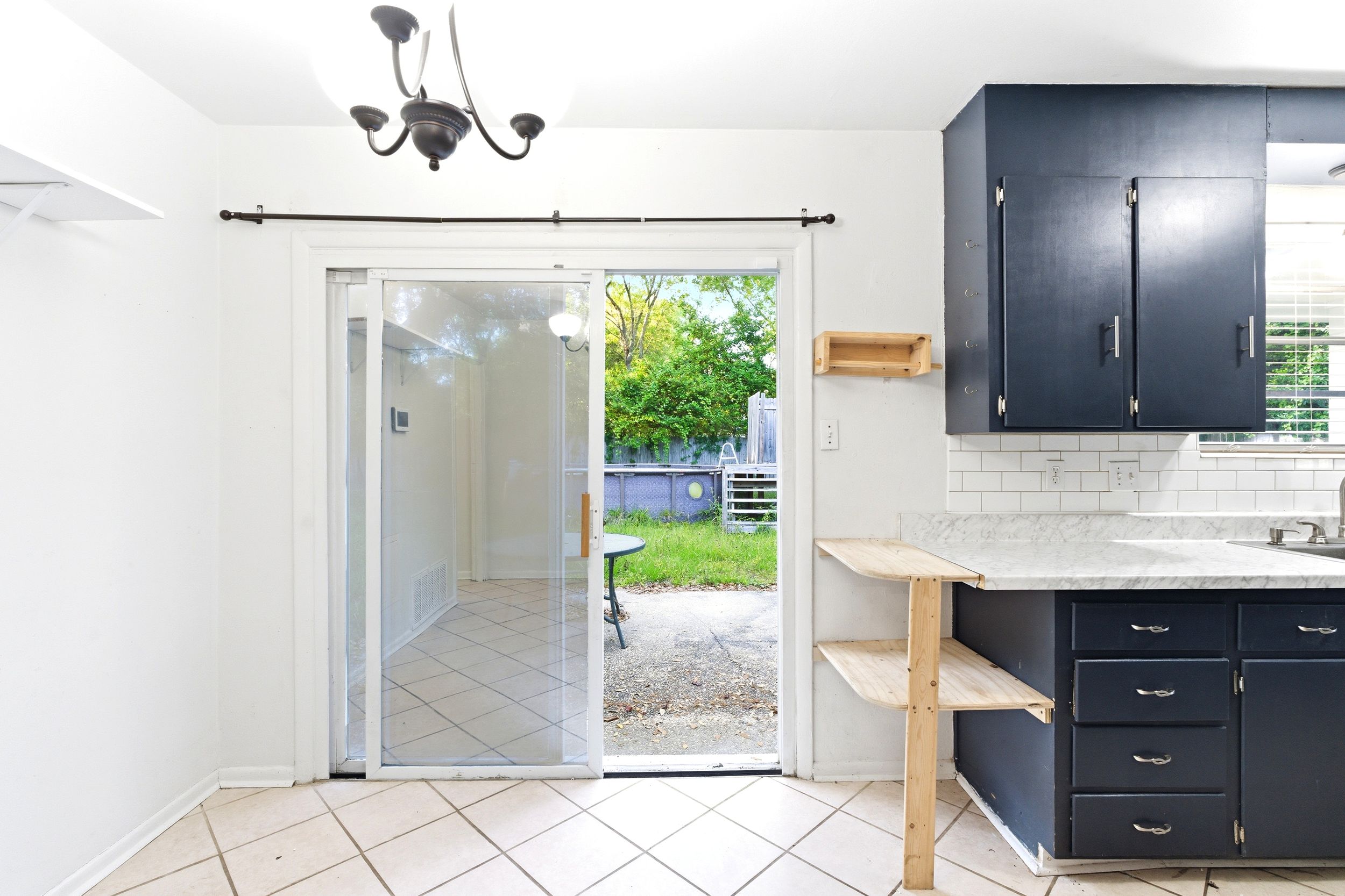 Kitchen with navy cabinets, subway tile backsplash, and sliding glass doors opening to a sunny backyard patio.