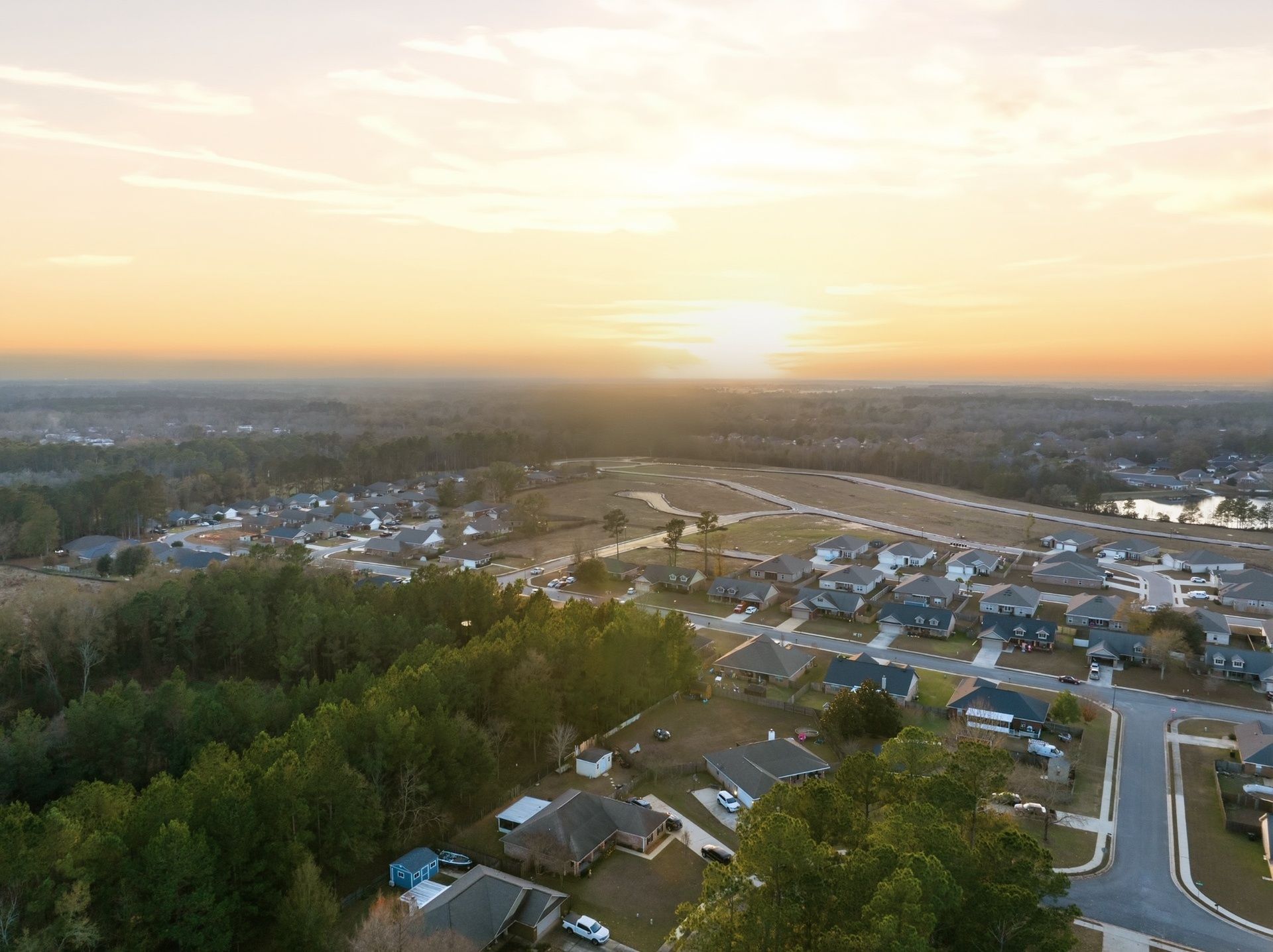 Aerial panoramic view of a suburban neighborhood development at sunset with winding streets and homes.