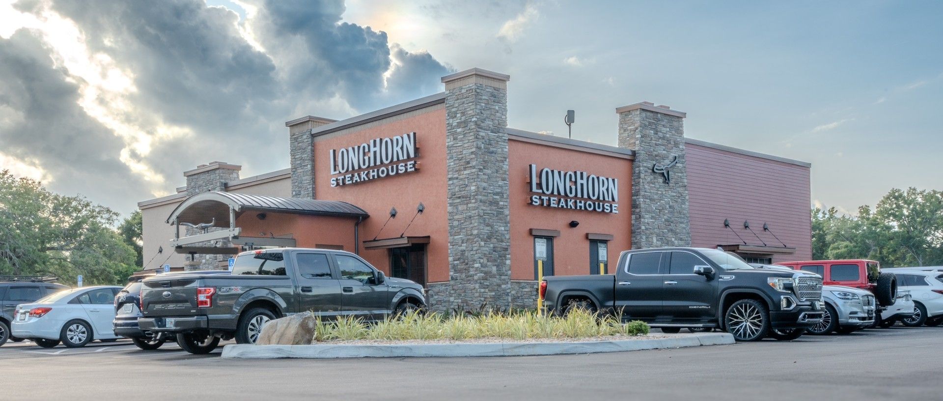 A Longhorn Steakhouse restaurant exterior with cars parked in front during sunset with cloudy skies.