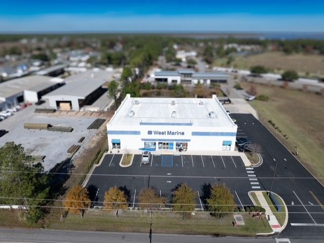 Aerial view of industrial buildings and warehouses with parking lots and surrounding landscape on a clear sunny day.