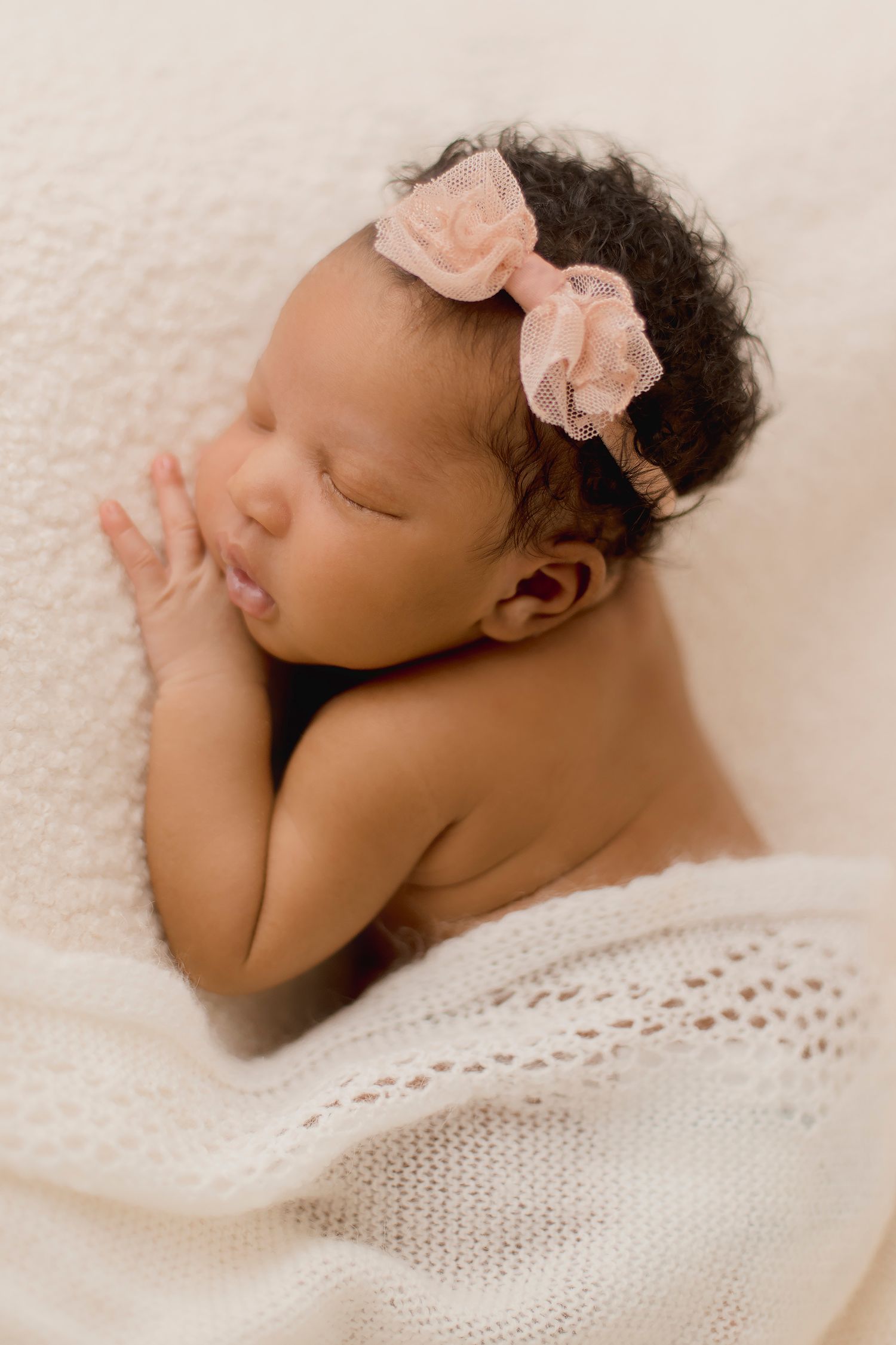 A sleeping newborn baby rests peacefully on soft gray fabric with delicate white lace details.