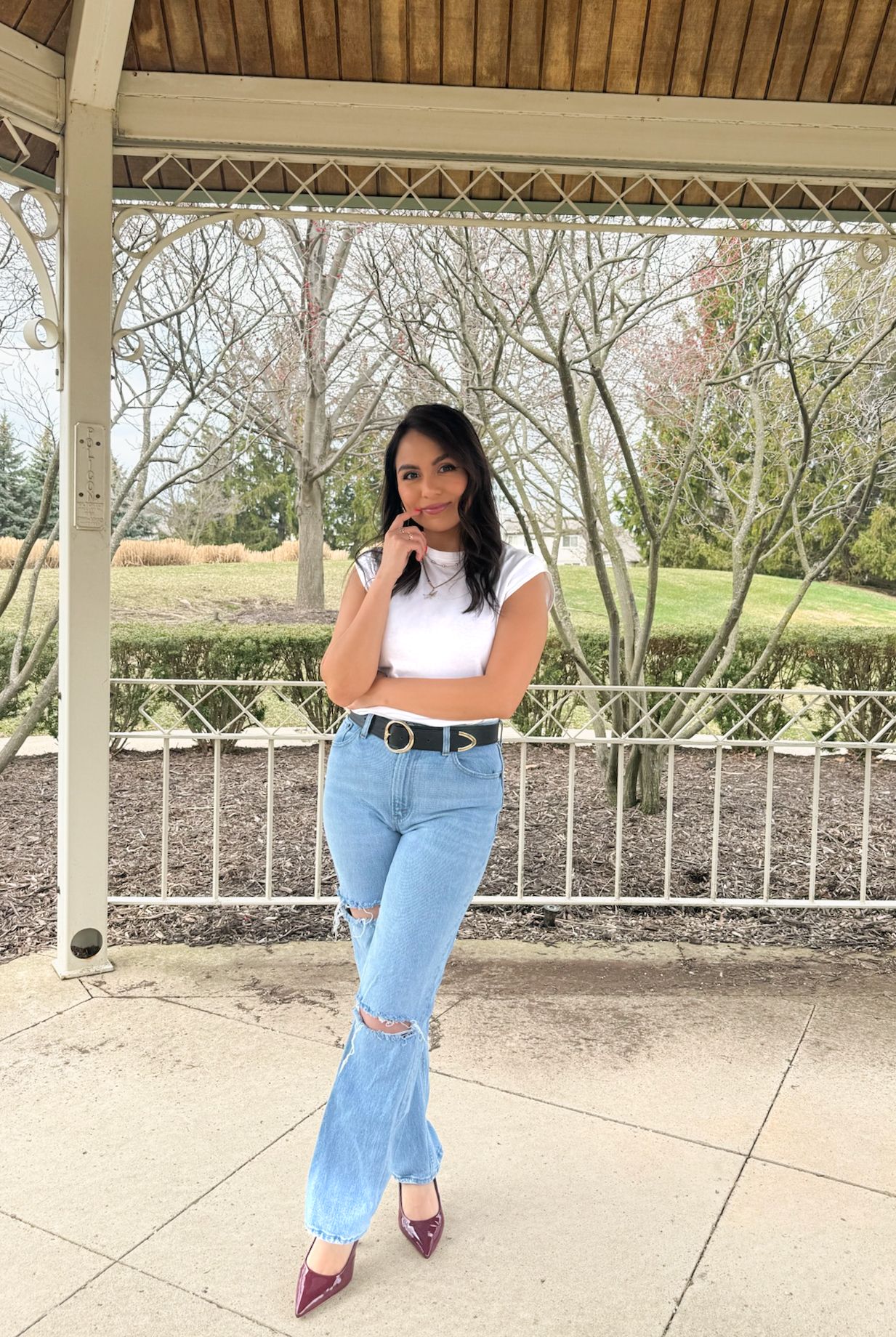 Person posing in casual denim outfit under a wooden pavilion structure.