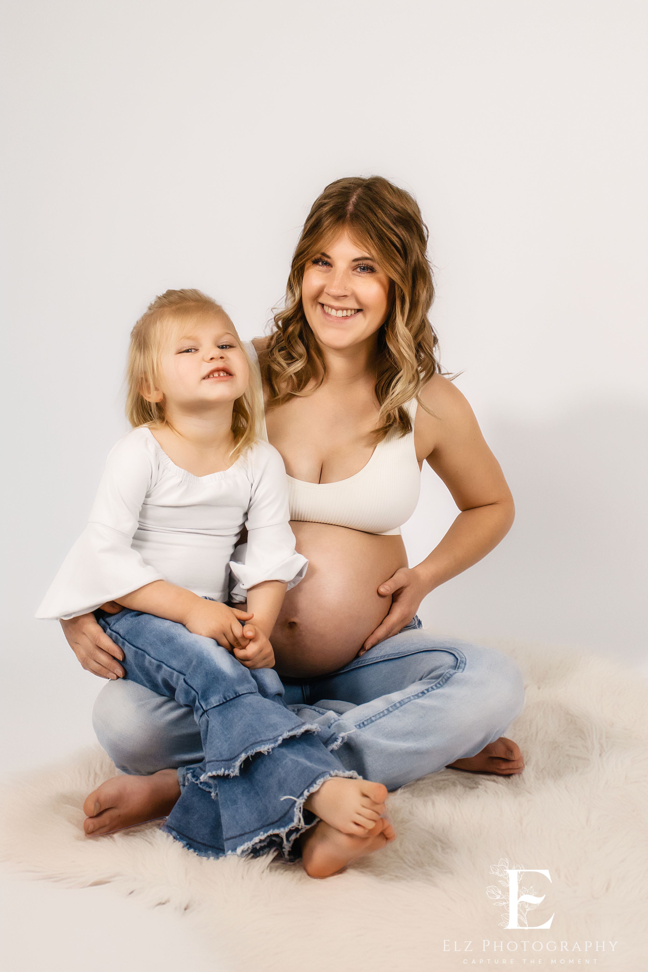 Studio maternity session with mother and child in casual attire against white backdrop in Williston, North Dakota.