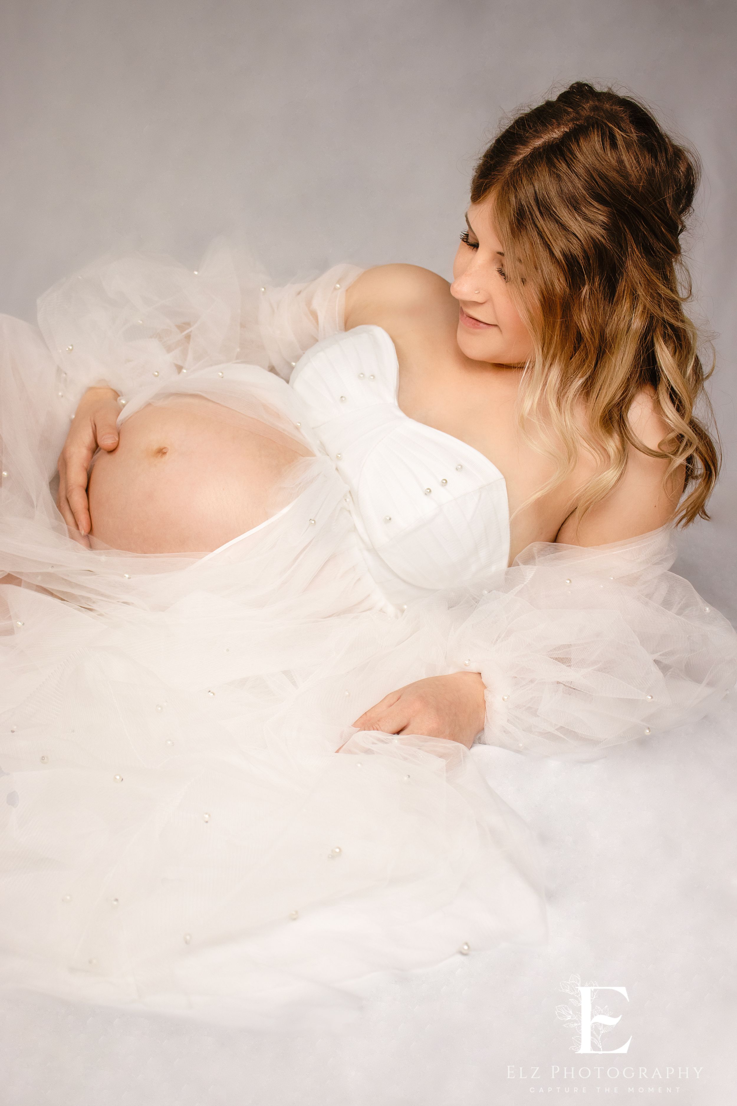 Dreamy maternity photos with flowing white tulle fabric against neutral studio background in Williston, North Dakota.