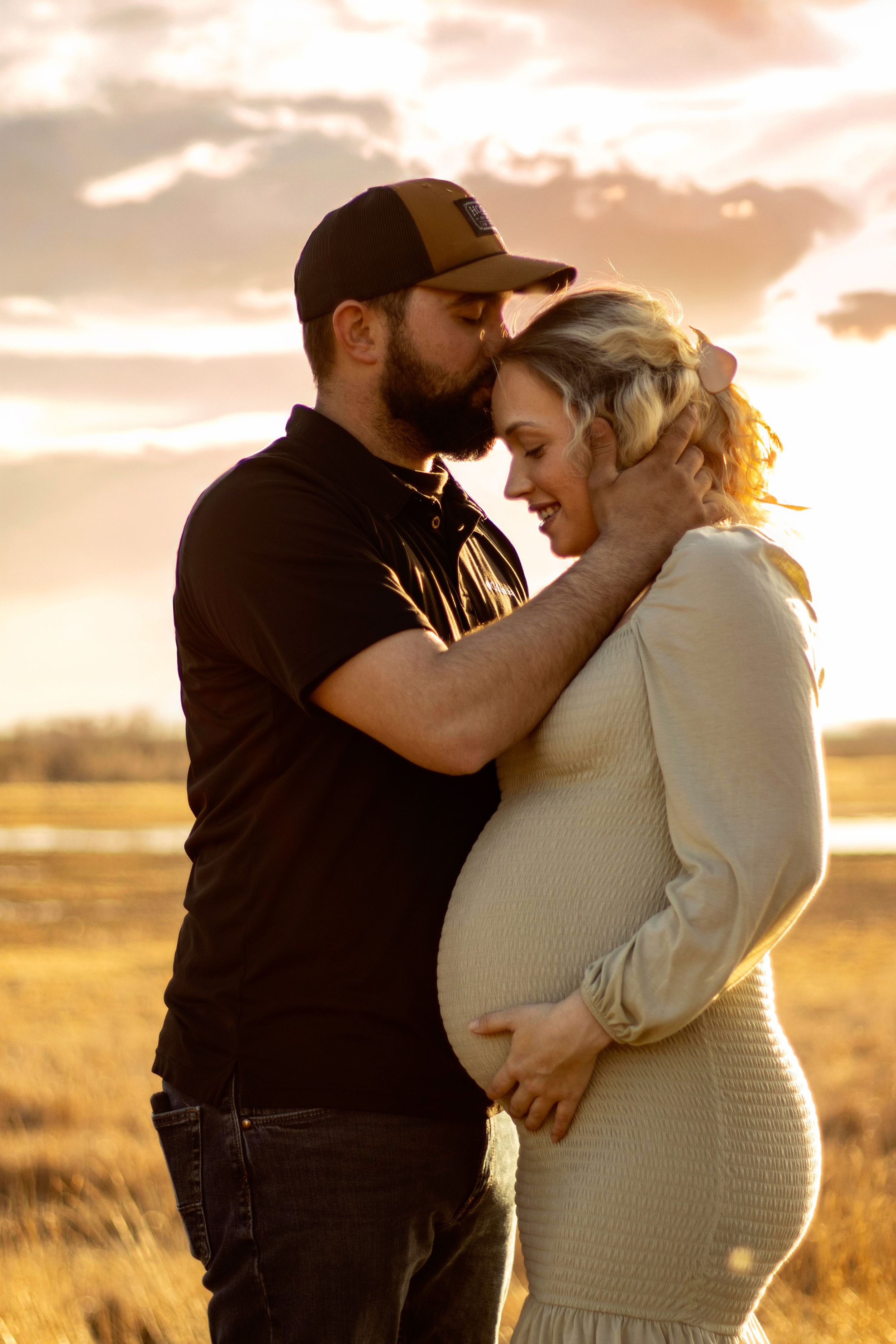 A romantic couple embraces in a golden wheat field during sunset creating a silhouetted maternity photo series in Williston, North Dakota.