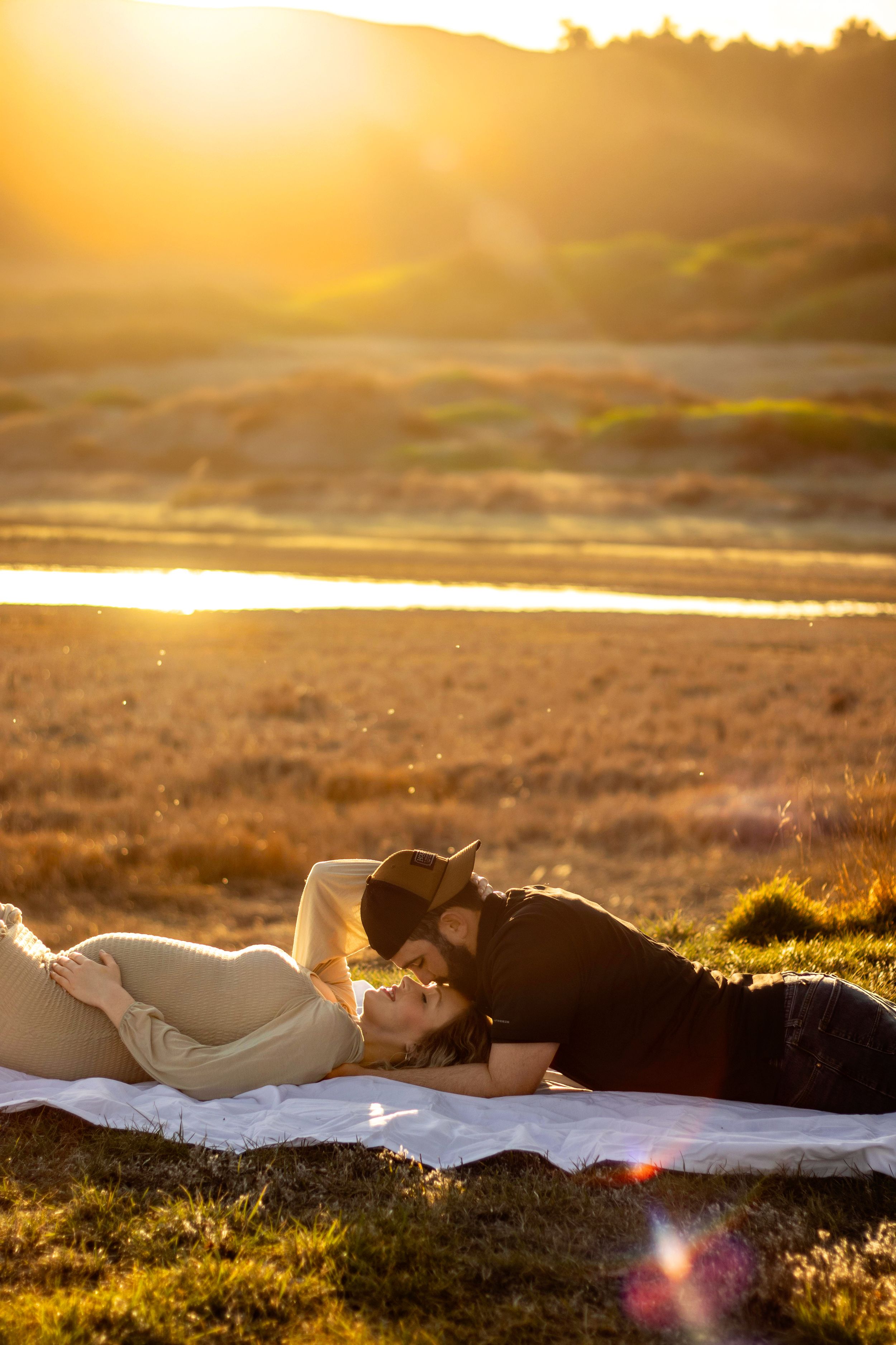 Romantic sunset maternity photo with couple lying in golden field in Williston, North Dakota.