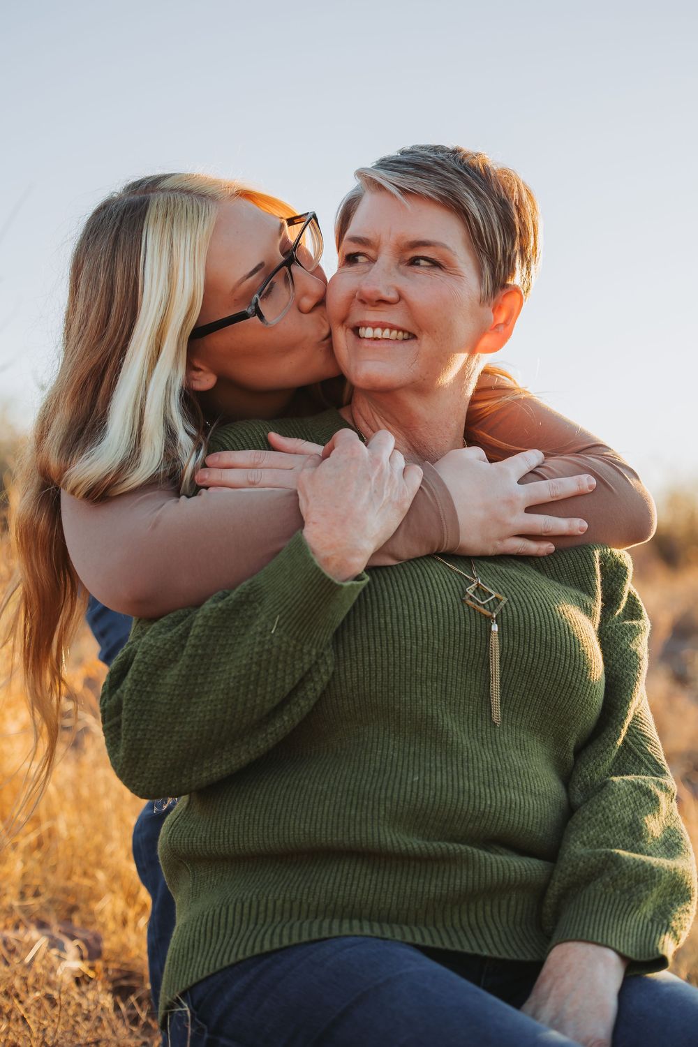 Two people share an intimate moment together in a golden field during sunset.