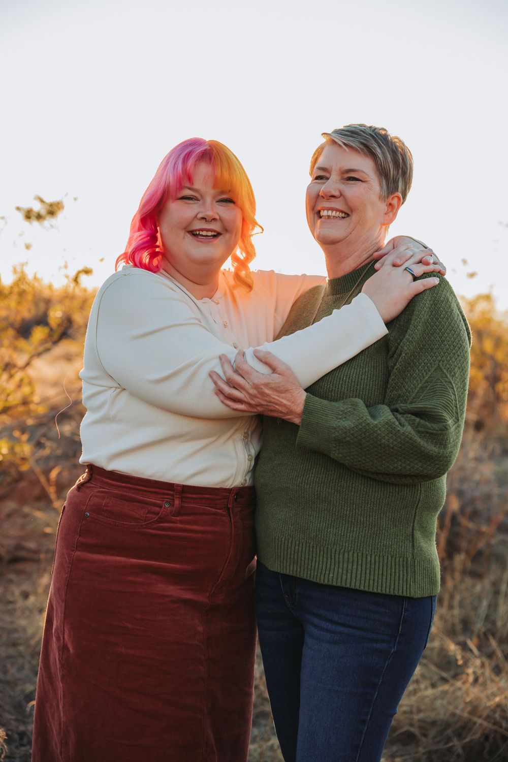 Two people share a joyful embrace while laughing together outdoors during golden hour sunset.