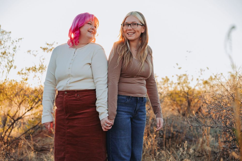 A couple stands together in a desert landscape during golden hour sunset.