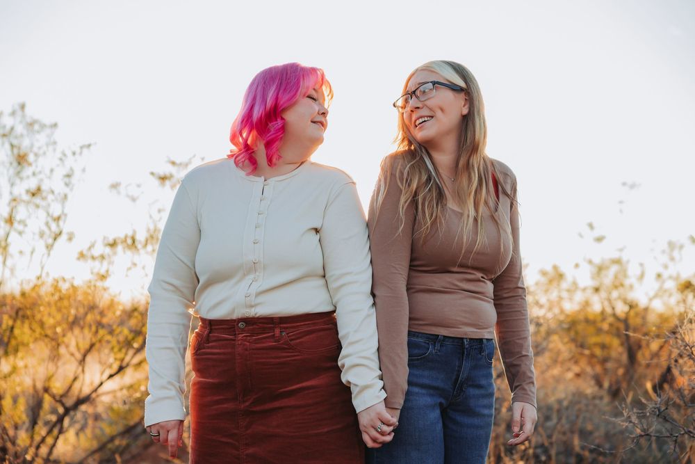 Two people hold hands while walking outdoors during golden hour sunset in an autumn landscape.