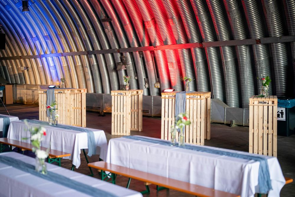 Indoor event space with curved ceiling illuminated by red and blue lighting showing rows of wooden seating.