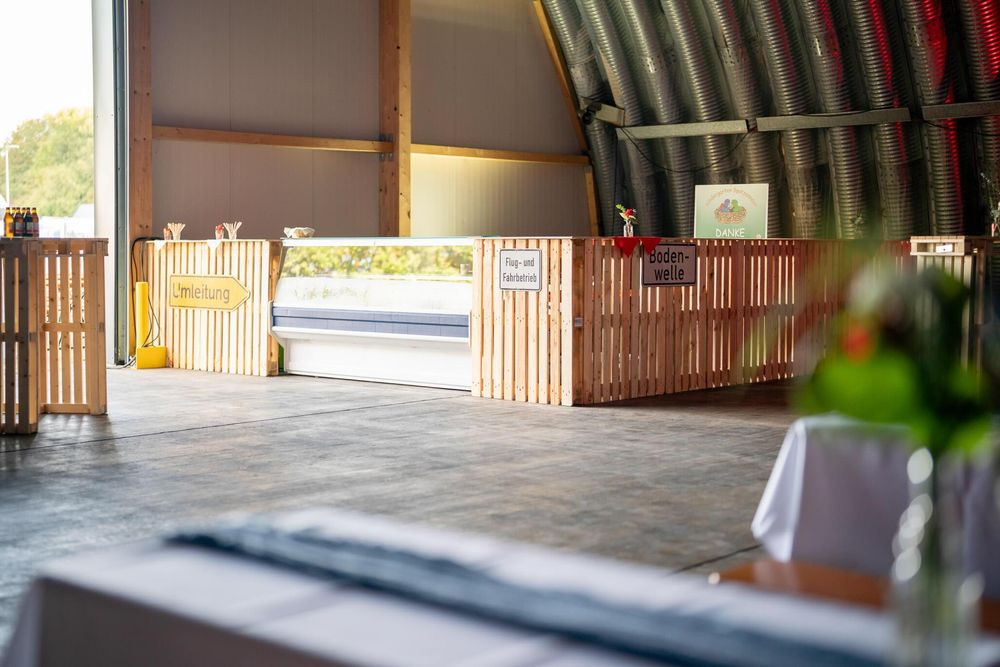 A wooden covered bridge with rustic timber beams spans across a scenic waterway in a natural setting.