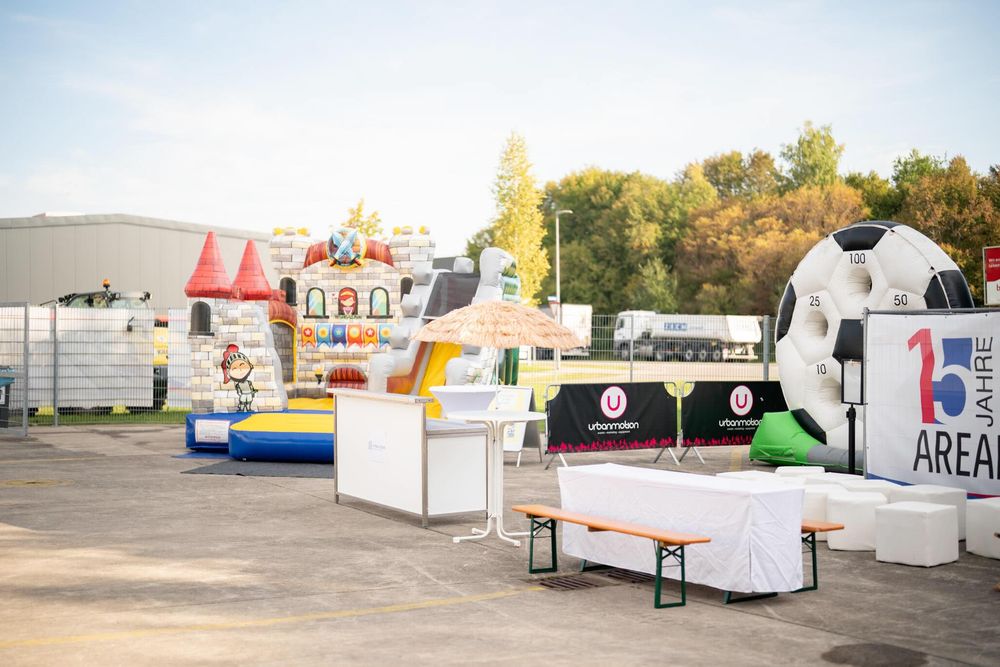 Colorful carnival game booths and inflatable attractions set up in an outdoor parking area on a sunny day.
