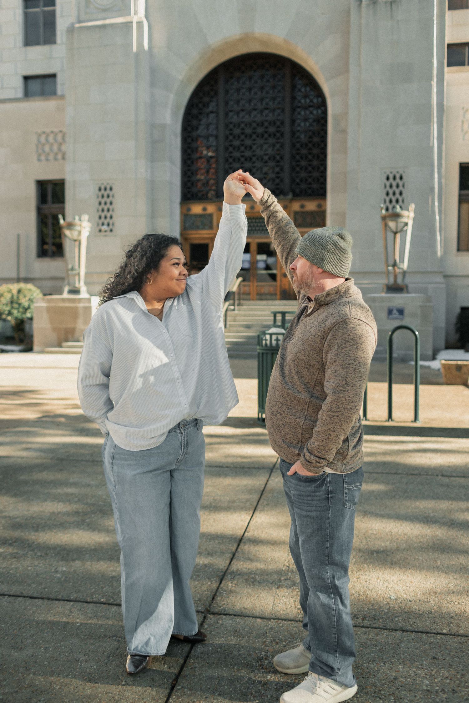 Two dancers perform an expressive contemporary dance routine in a courtyard with arched architecture in the background.