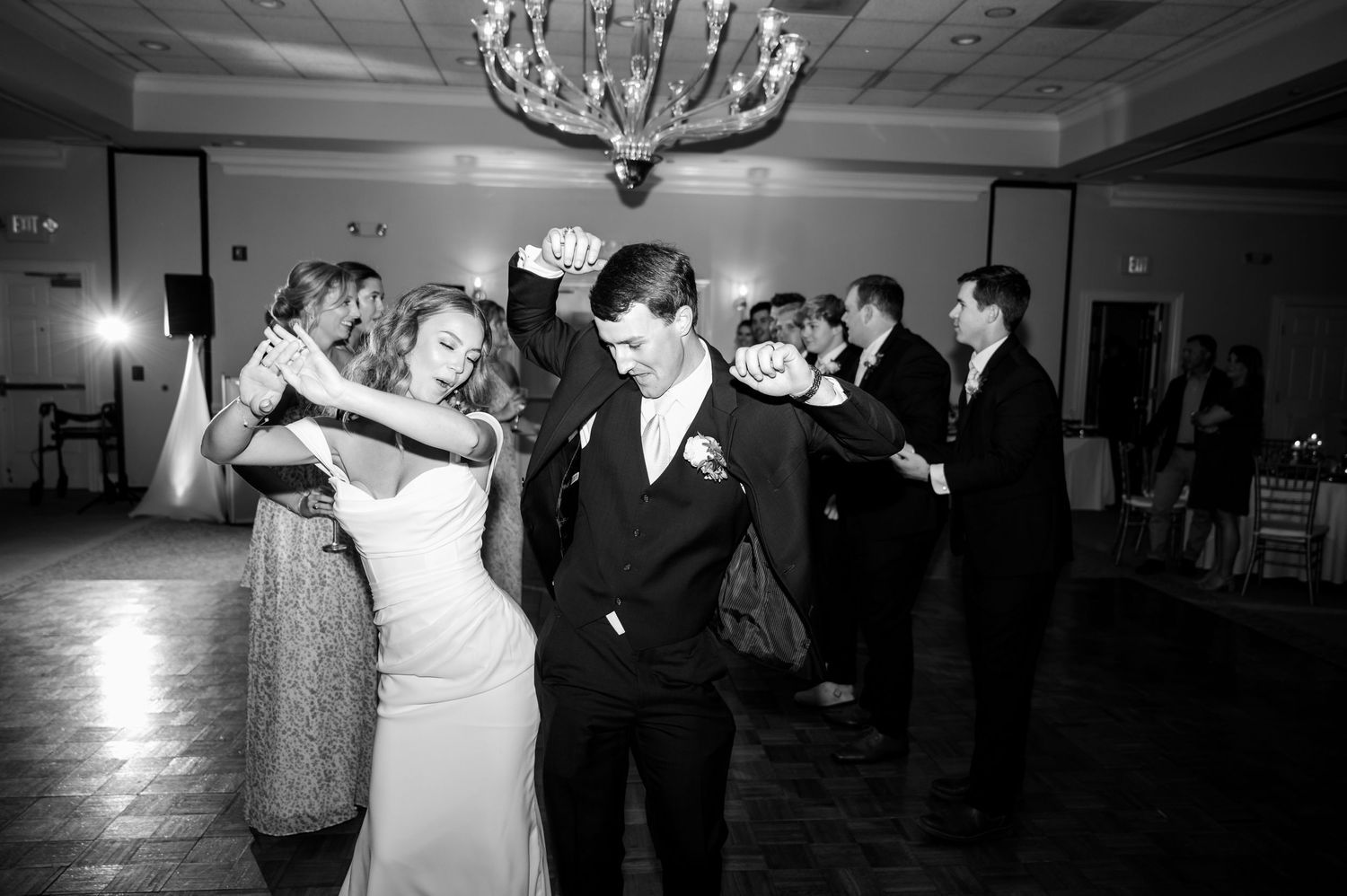 Wedding reception dance floor scene with chandelier lighting and guests dancing in formal attire.