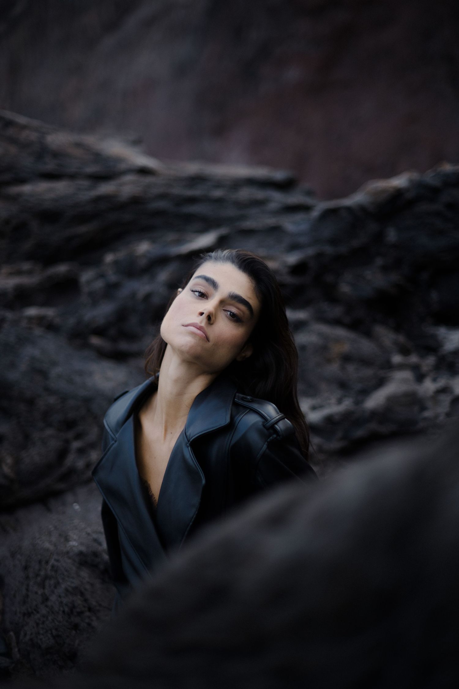 Artistic portrait of someone in a black jacket against dark rocky terrain at dusk.