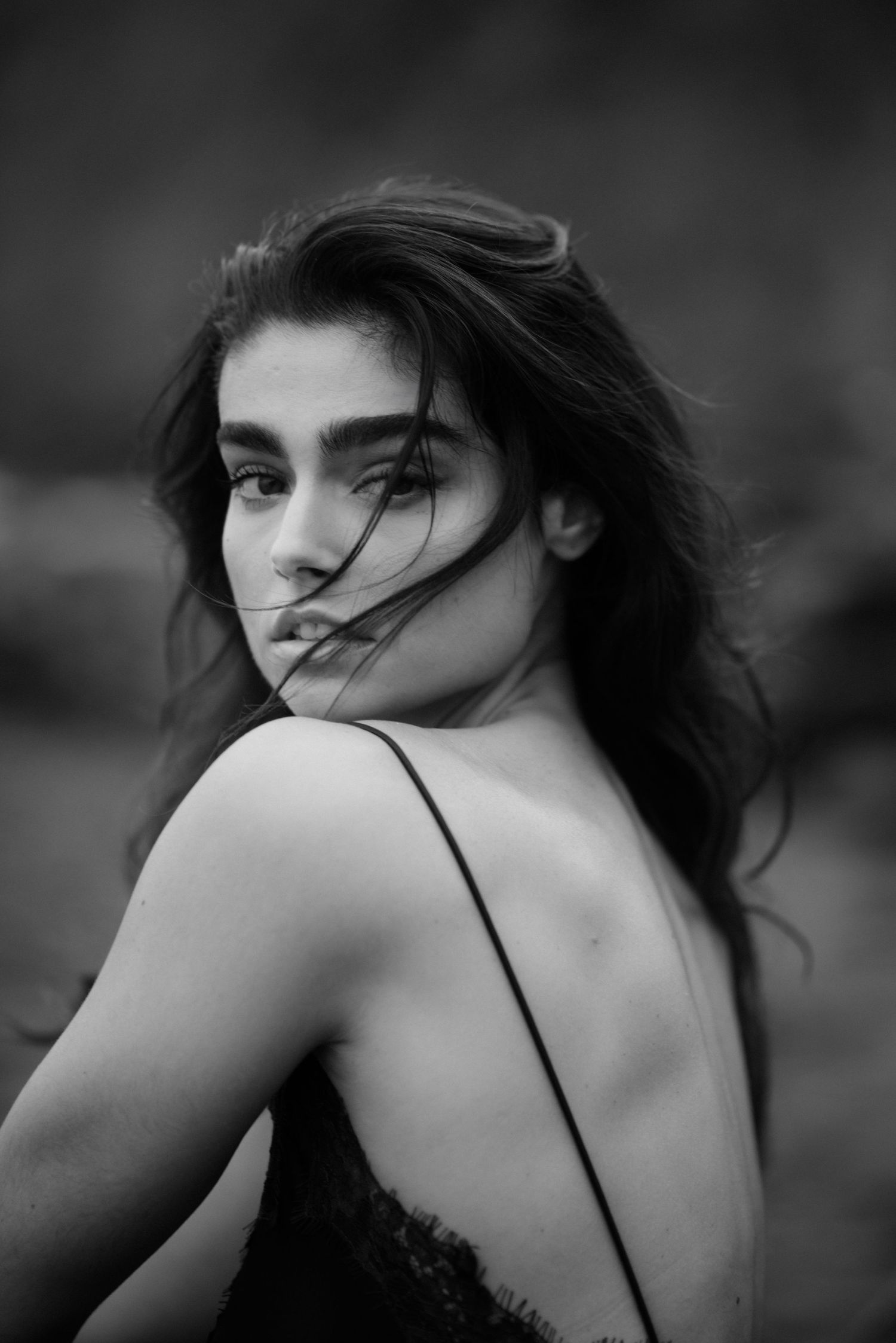Black and white portrait of a person with flowing dark hair looking over their shoulder in a delicate lace top.