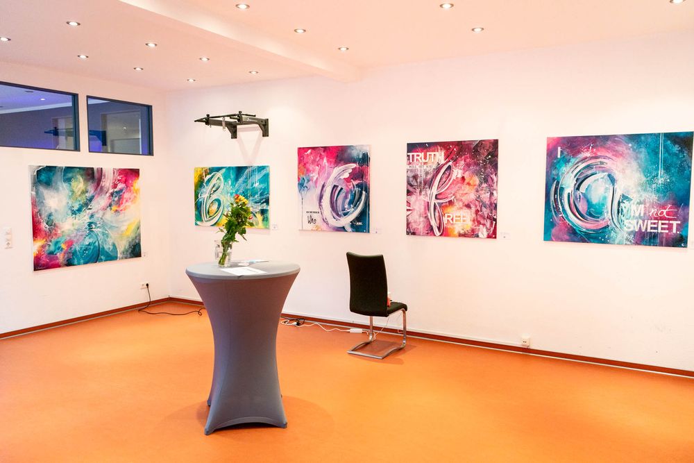 Modern art gallery space with vibrant colorful abstract prints on white walls and an orange floor with minimalist furniture.